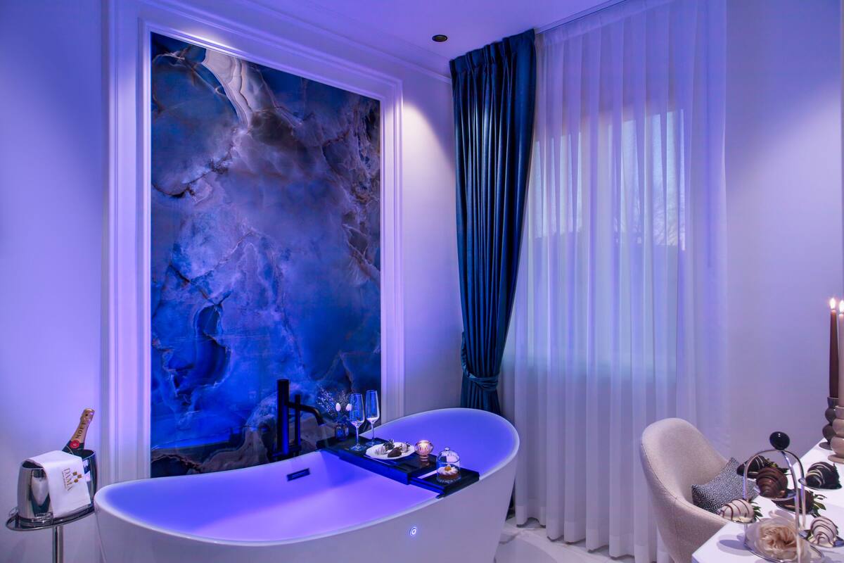 Une salle de bain moderne avec une baignoire sur pieds, un grand tableau abstrait et un coin salon avec une table dressée pour un repas.