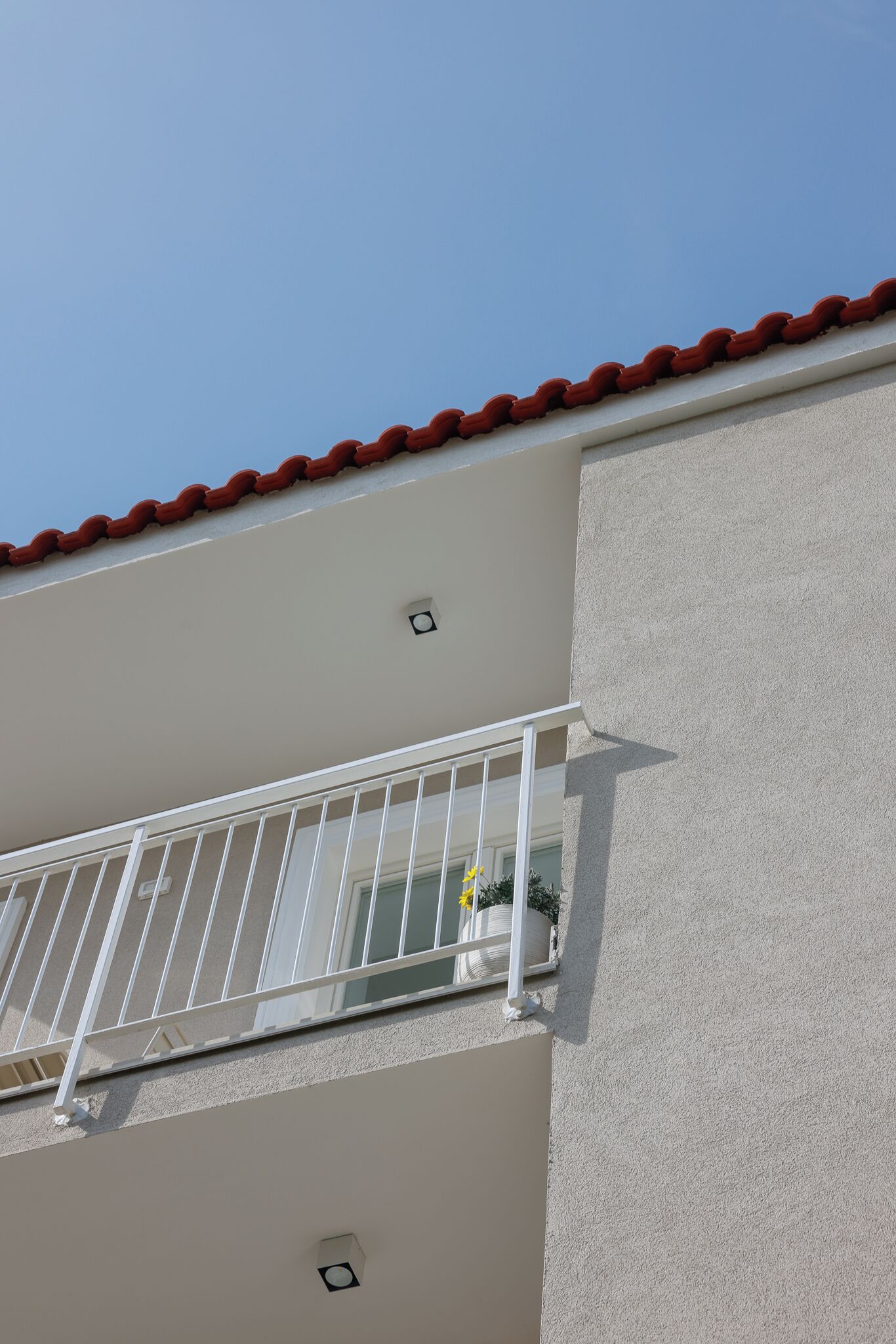 Un edificio con techo de tejas rojas, barandal de balcón blanco y pared exterior blanca.