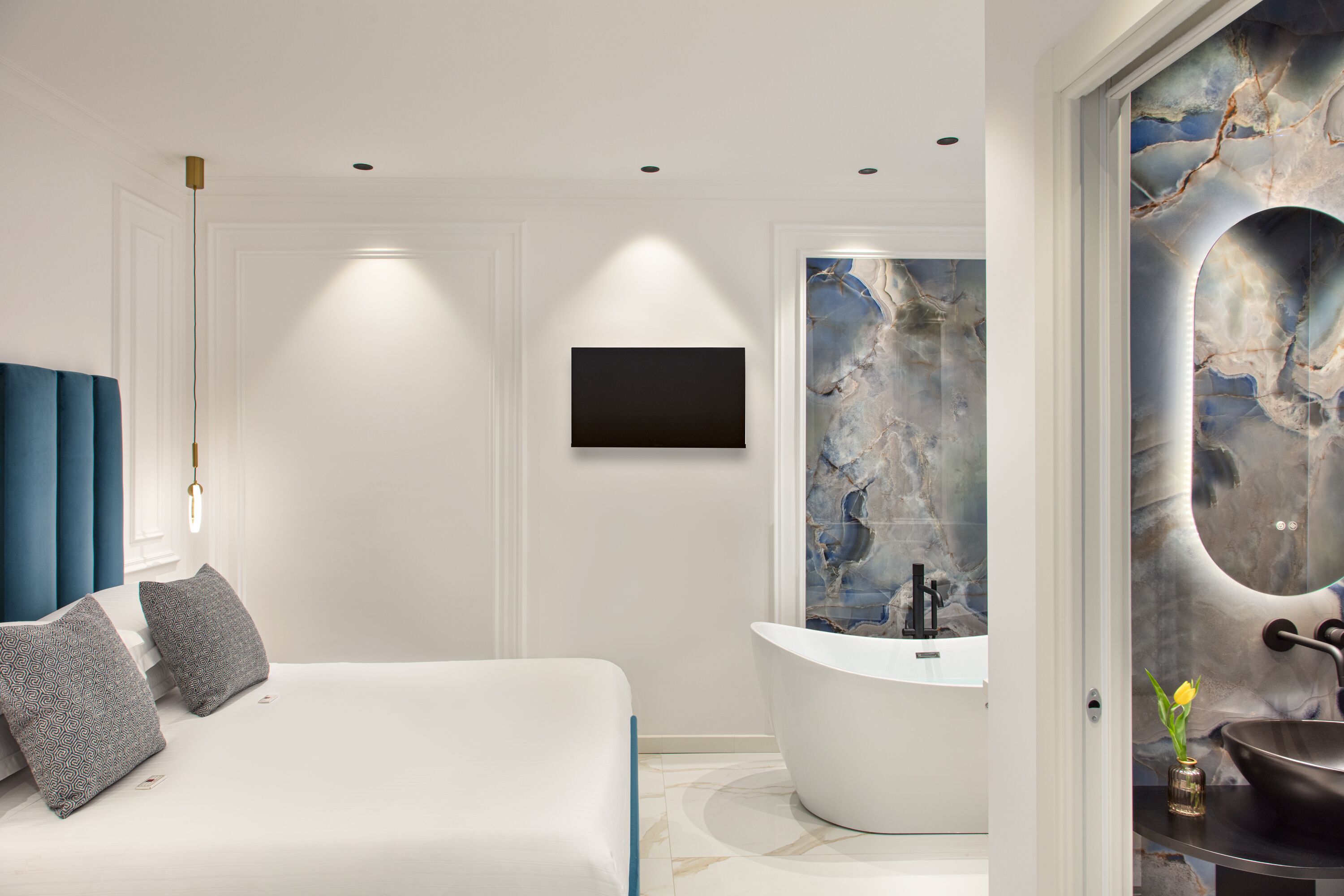 A modern bedroom with a large bed, a flat-screen TV, a marble wall, and a freestanding bathtub.