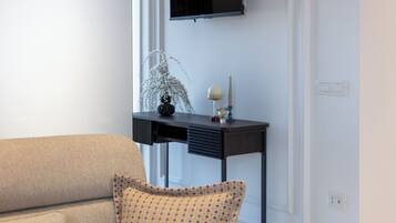 Una sala moderna con un sofá color beige, un sillón estampado, una mesita de noche de madera oscura y un televisor montado en la pared.