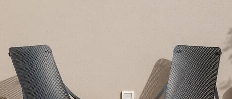 Deux chaises en métal noir, dotées d’un dossier et de pieds perforés, sont placées contre un mur beige, à proximité d’un petit interrupteur blanc.