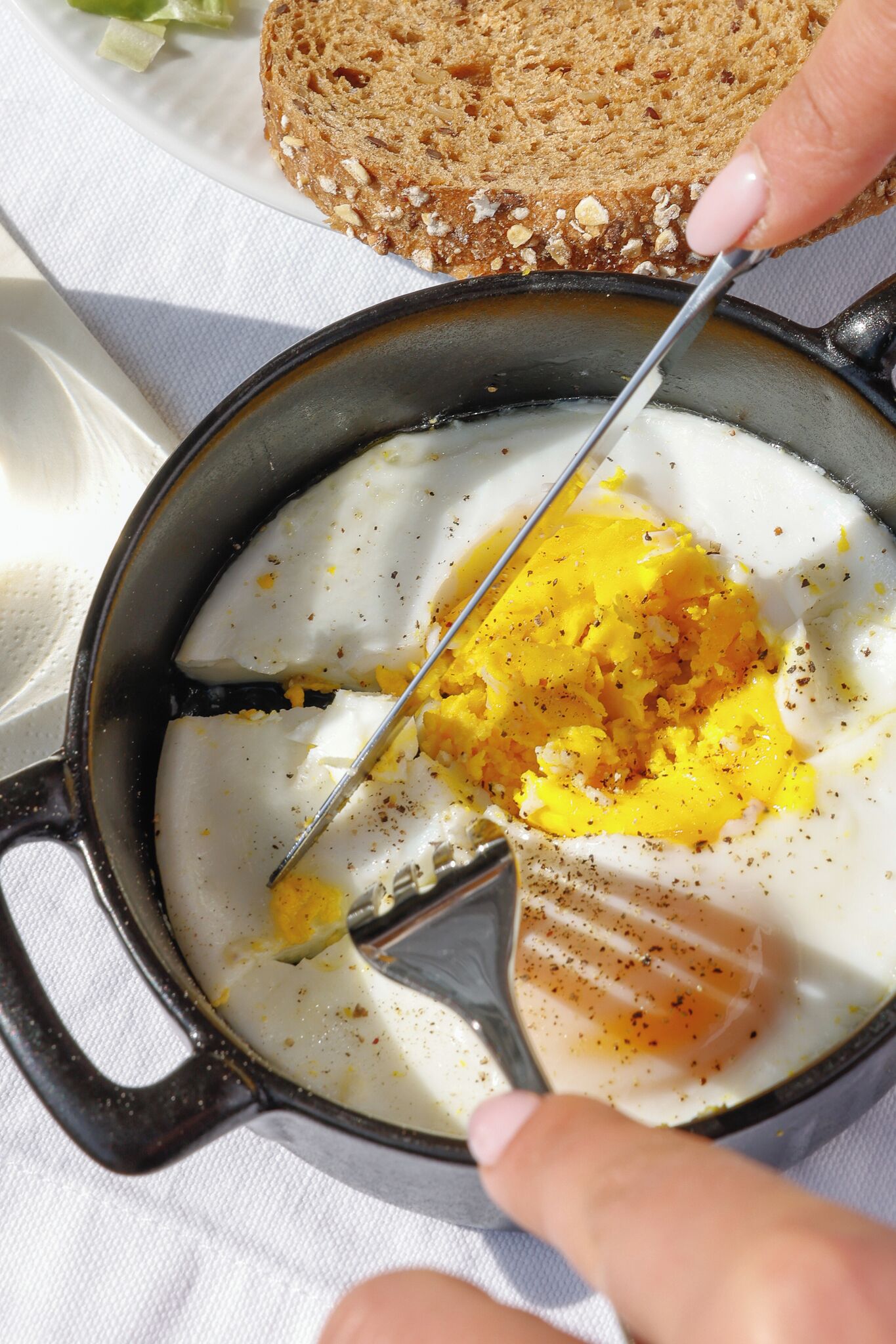 Una sartén con huevos revueltos y una rebanada de tostada sobre un paño blanco.