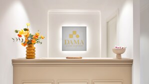 Een receptiebalie met een lijst waarop staat 'DAMA LUXURY APARTMENT' en een bloemenvaas aan de linkerkant.