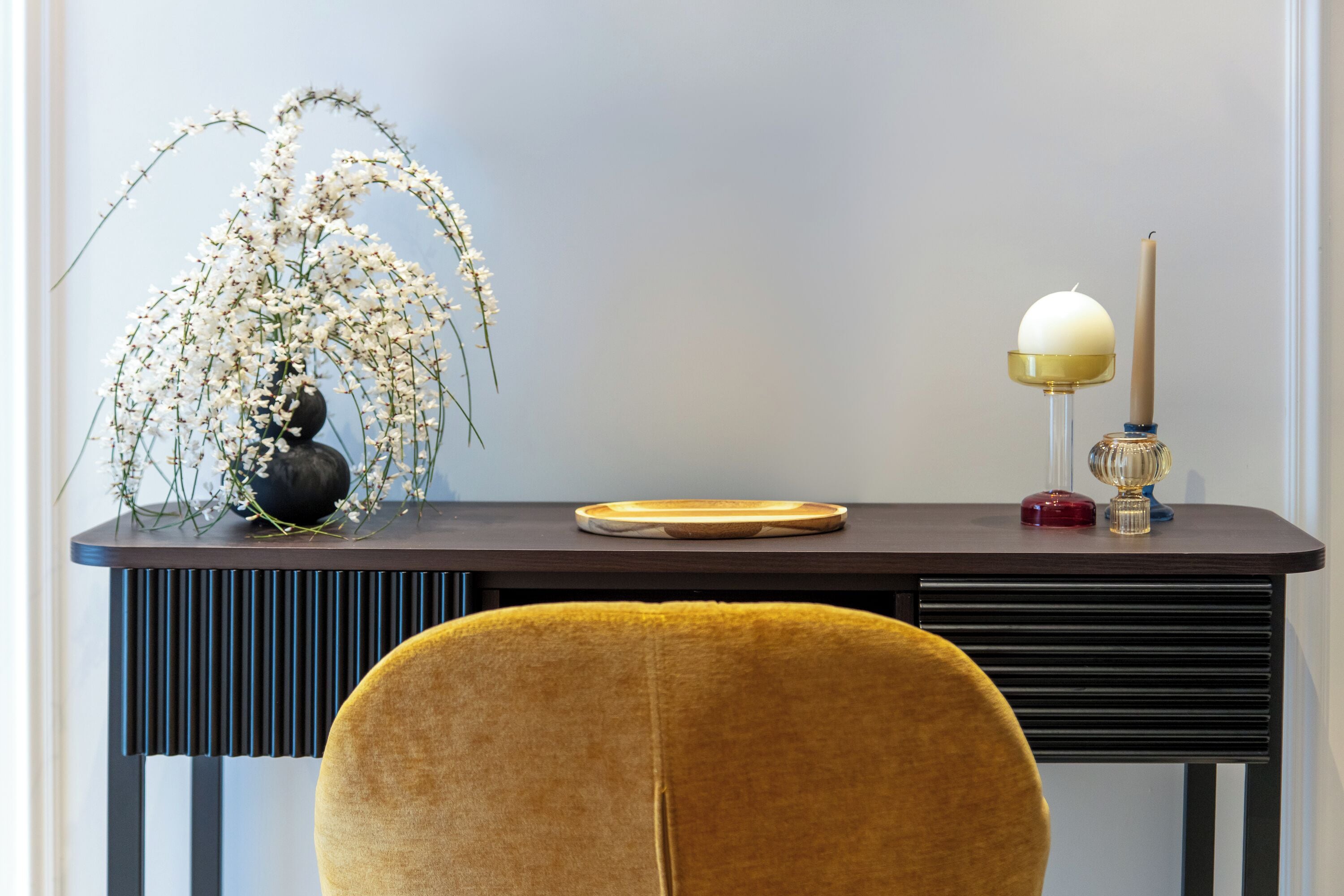 A modern desk with a vase of white flowers, a candle, and a decorative plate.