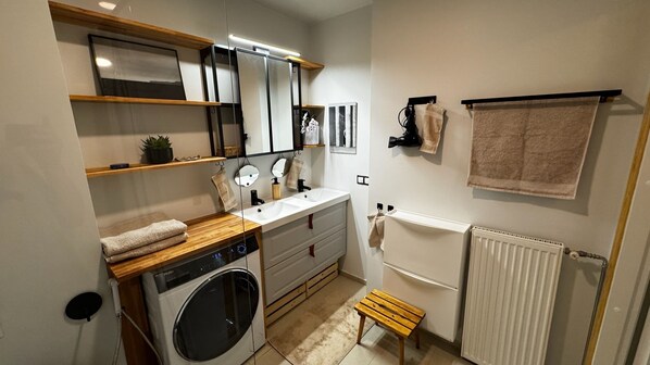 A compact bathroom with a washing machine, a sink, a mirror, and a towel rack.