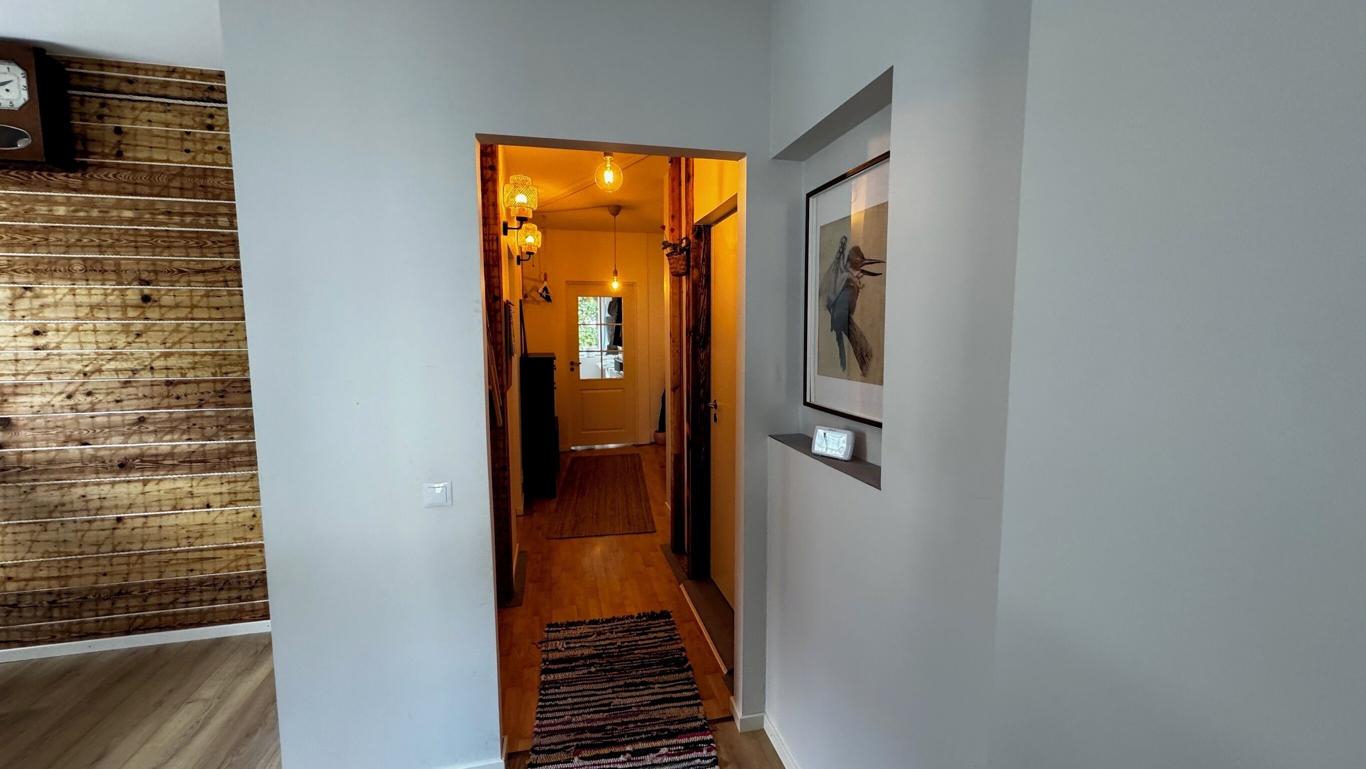 Ein Flur mit einer Holzwand, einer zur Kammer führenden Tür und einem gerahmten Bild an der Wand.