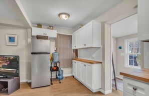 Cocina compacta con armarios blancos, refrigerador de acero inoxidable, encimera de madera y televisor sobre un mueble.