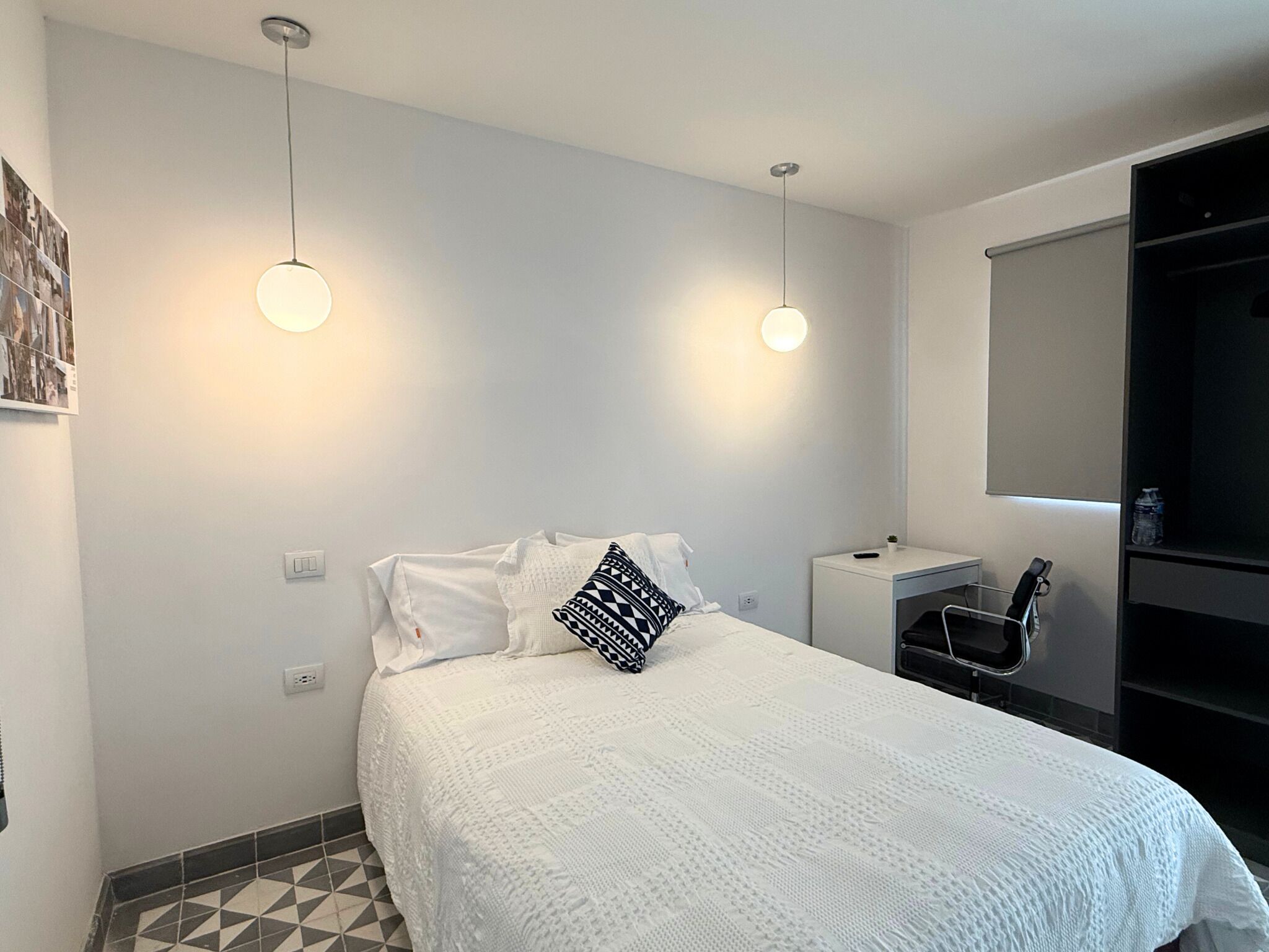 A modern bedroom with a white bed, geometric patterned pillows, a small bedside table, and a built-in wardrobe.