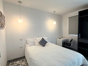 Un dormitorio moderno con una cama blanca, almohadas de estampado geométrico, una mesita de noche pequeña y un armario empotrado.