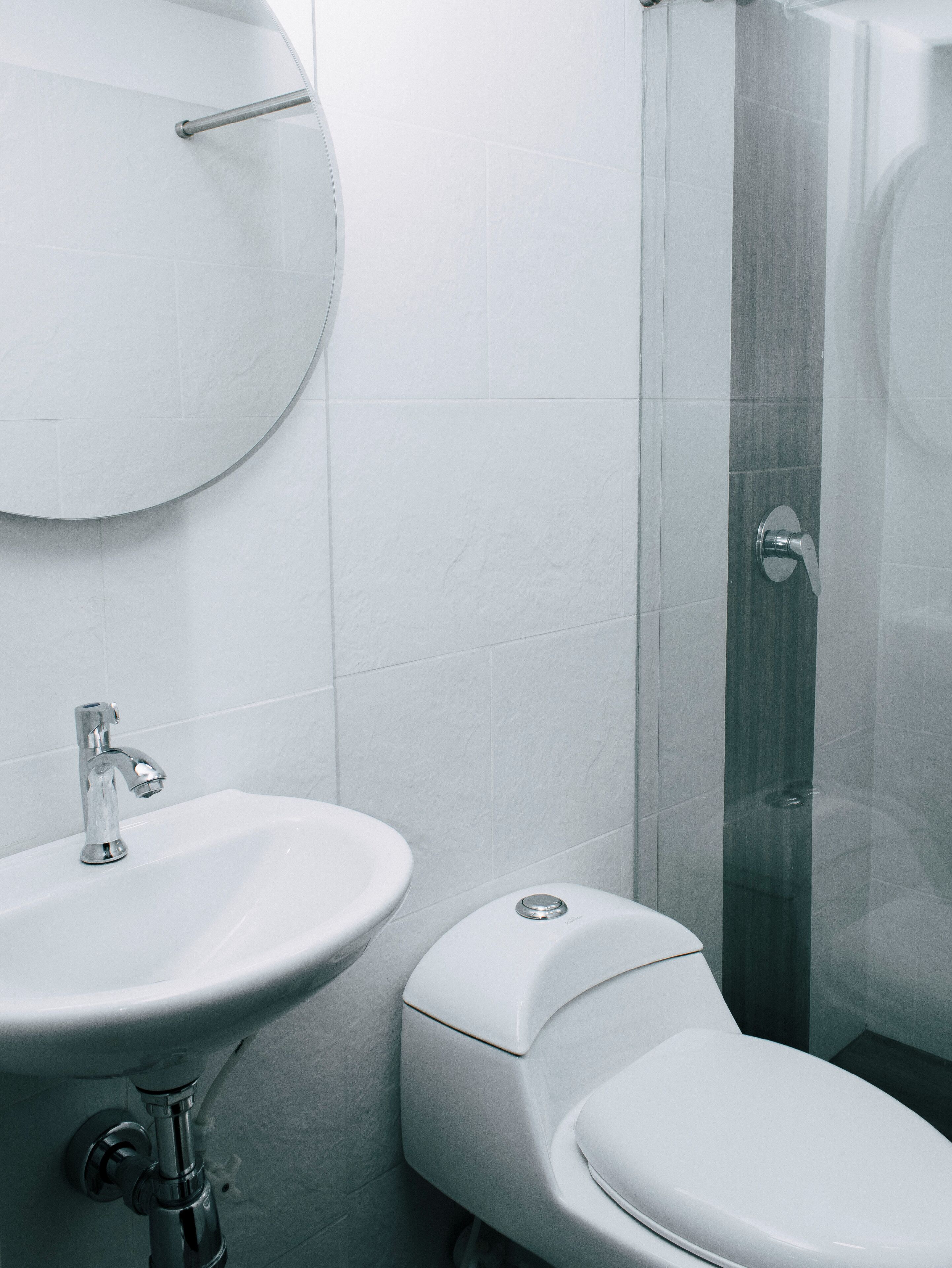 A modern bathroom with a round mirror, a sink, and a toilet.