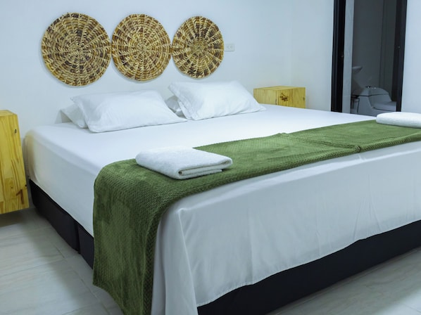 A neatly made bed with white linens, a green throw blanket, and a white towel. There are three woven wall decorations above the bed. - Casa Lupe Hostal (Envigado)