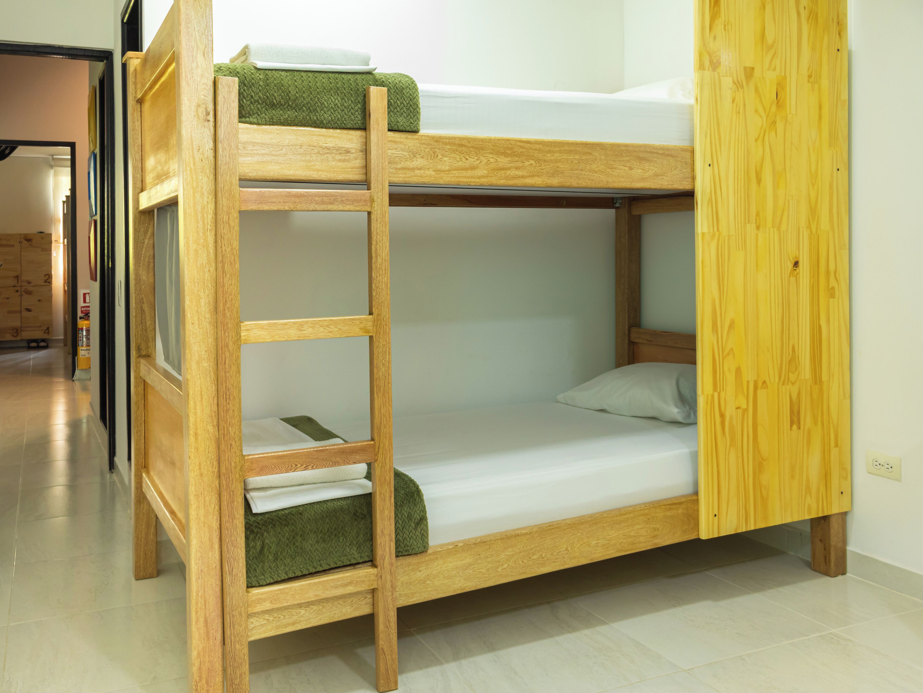 A bunk bed with a wooden frame, a green blanket, and a white mattress.
