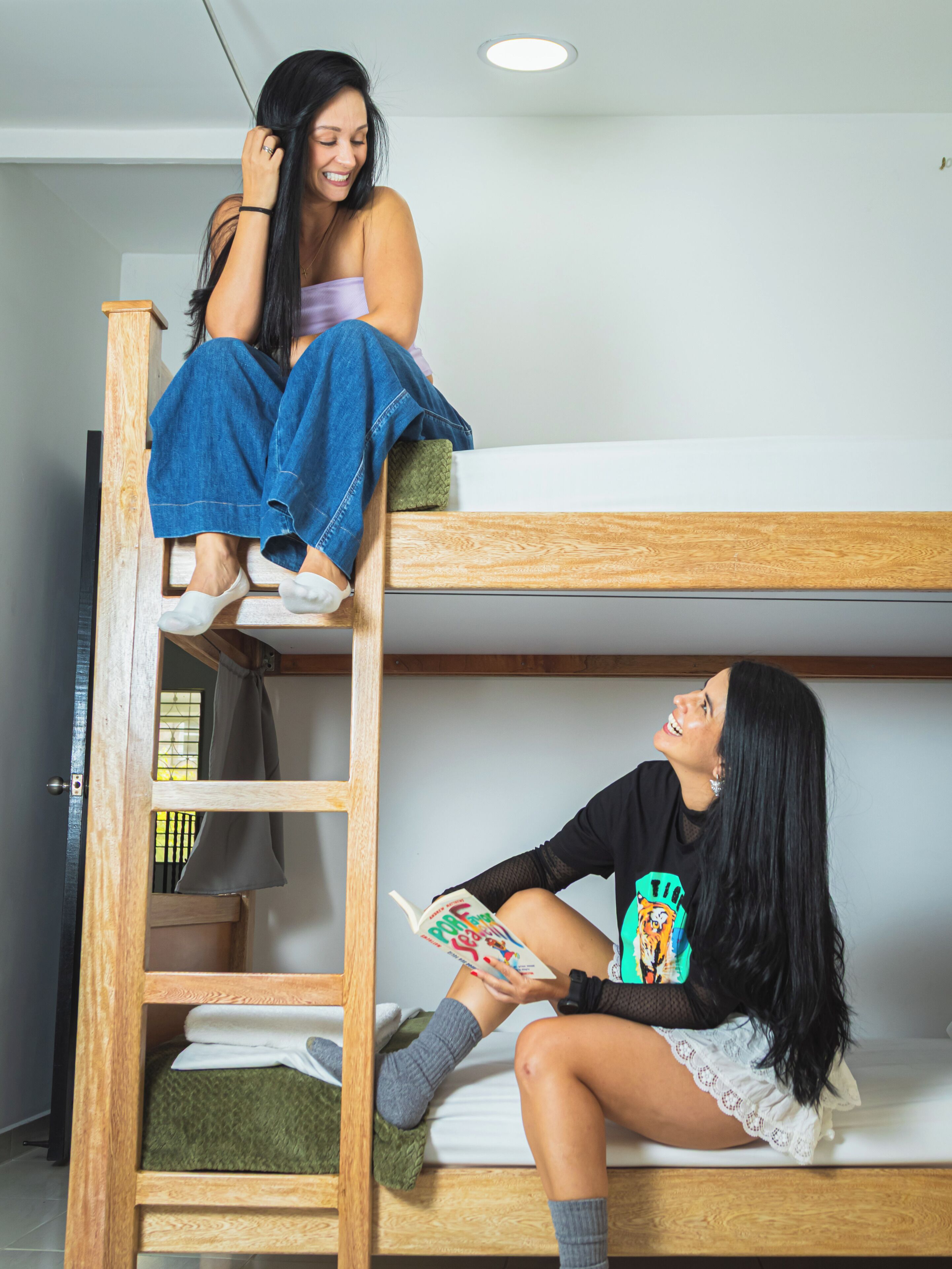 A bunk bed room with a ladder, a green pillow, and a person reading a book.