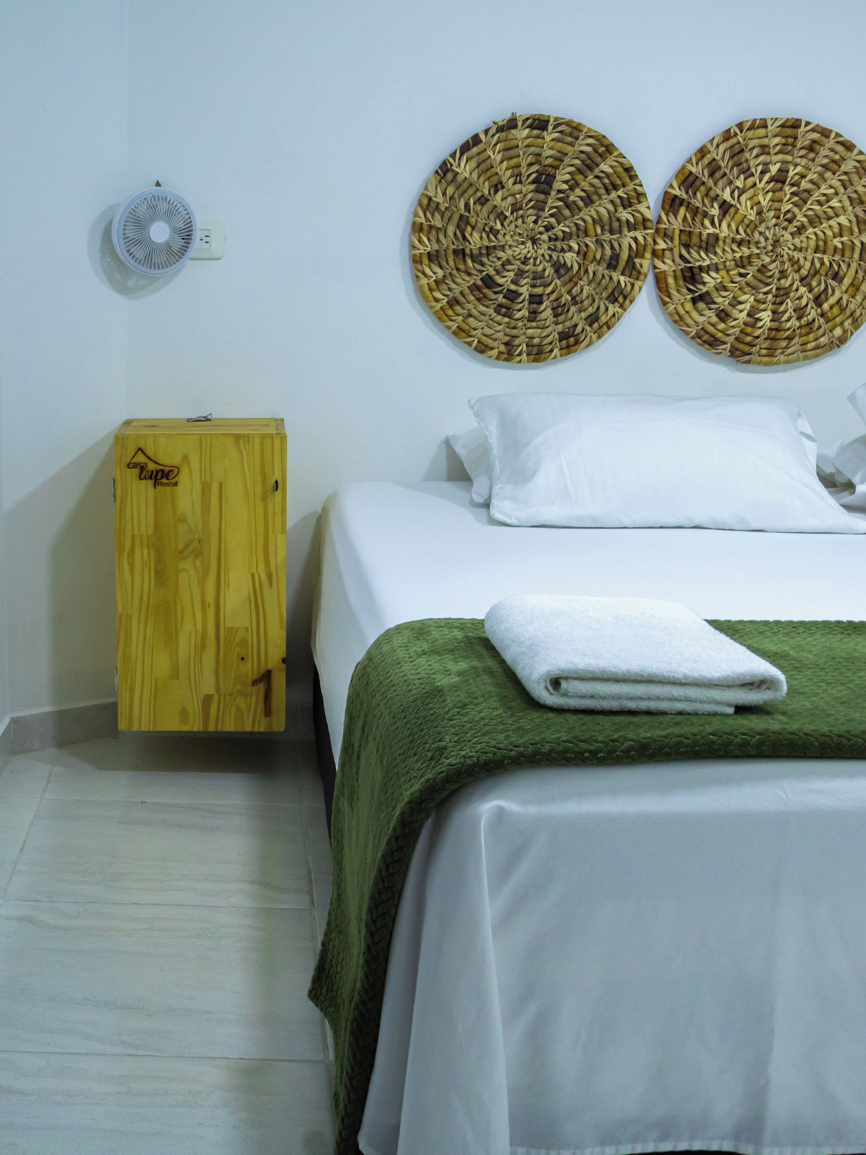 A hotel room with a bed, a wooden cabinet, two woven wall decorations, and a white pillow.