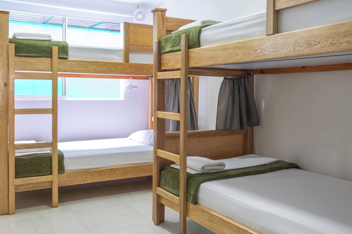 Une chambre avec un lit superposé, des montants en bois, du linge de lit blanc et une fenêtre avec des rideaux.