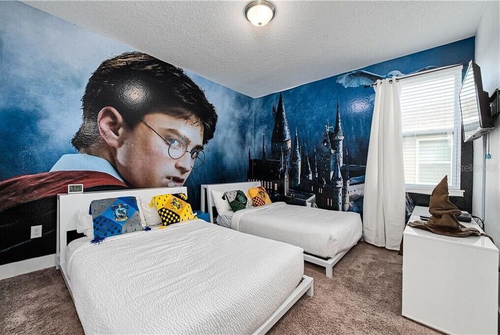 Une chambre avec deux lits, une grande affiche représentant un magicien accrochée au mur et une fenêtre avec des rideaux.