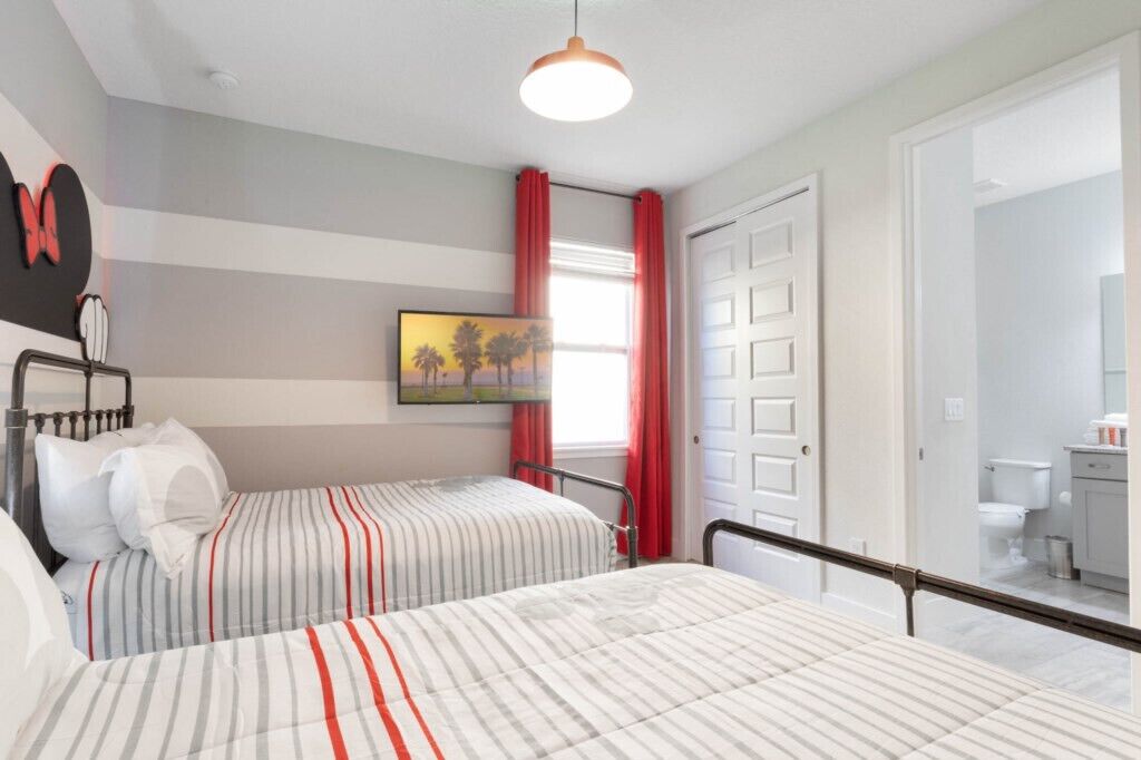 A bedroom with two beds, a painting, and a bathroom visible through an open door.