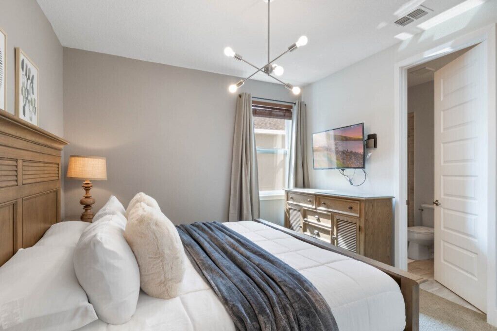 A bedroom with a bed, bedside lamp, dresser, and a TV mounted on the wall.