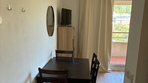 A dining area with a table and chairs, a television on a cabinet, and a view of the outside through a window. - 302, LE VIRGINIA, near the center of Grasse (Grasse)