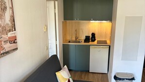 A compact living space with a dark grey sofa, a small kitchenette, and a trash bin. - 302, LE VIRGINIA, near the center of Grasse (Grasse)
