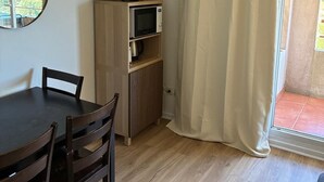 A room with a dining table, chairs, a television on a wooden cabinet, a microwave, and a large window with curtains. - 302, LE VIRGINIA, near the center of Grasse (Grasse)