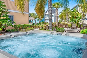 A hot tub surrounded by lush greenery and a poolside area with lounge chairs.