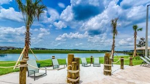 A poolside area with lounge chairs and wooden posts, a clear sky, and a body of water in the background.