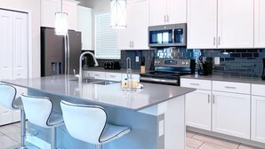 A modern kitchen with white cabinets, stainless steel appliances, and a central island with bar stools.