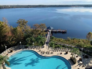 A swimming pool with a deck, surrounded by lounge chairs and palm trees, overlooking a large body of water.