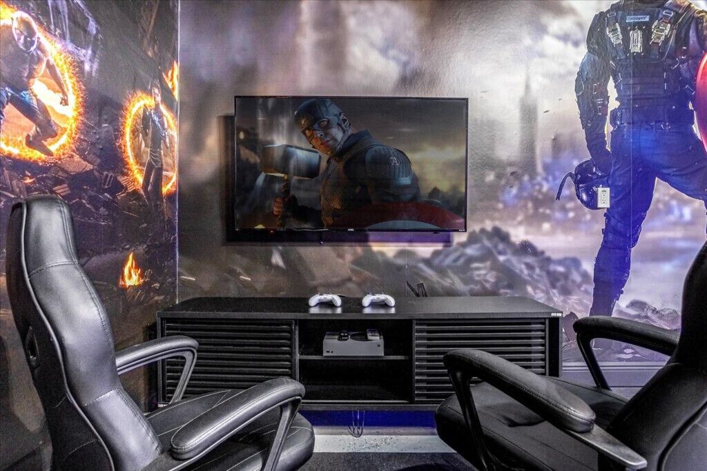 Una configuración para videojuegos con un televisor grande, dos sillas gamer y una consola.