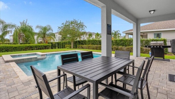 A covered outdoor area with a pool, a table and chairs, and a barbecue grill. - Last Minute Disney! Private Pool, Hot Tub & Themed Bedrooms. Book Now! #91365 (Orlando)
