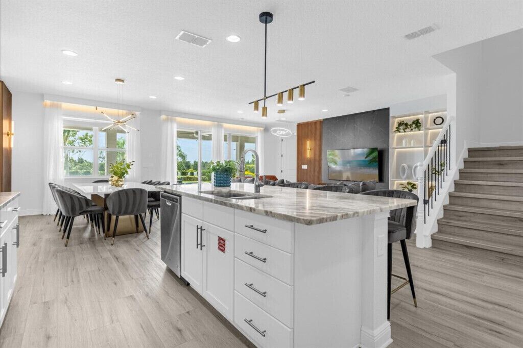 A modern kitchen with a large island, white cabinetry, and a dining area with a table and chairs.