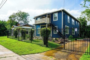 A two-story residential house with a balcony, a fenced yard, and a well-maintained lawn.