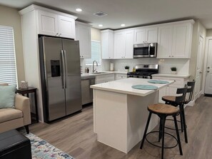 A modern kitchen with white cabinetry, stainless steel appliances, and a central island with bar stools.