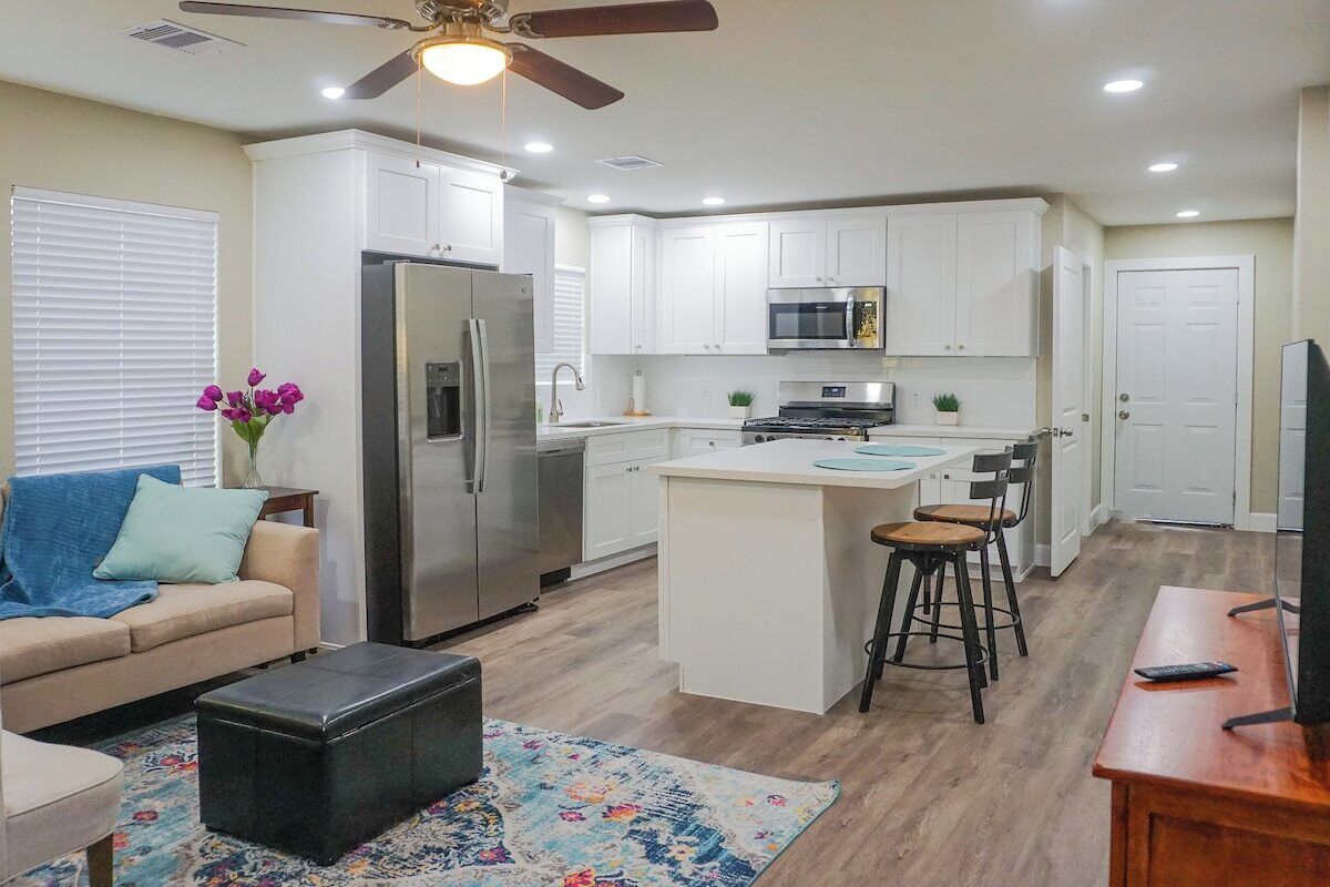 A modern kitchen with white cabinets, a stainless steel refrigerator, a microwave, and a central island with bar stools.