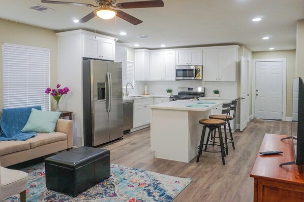 A modern kitchen with white cabinets, a stainless steel refrigerator, a microwave, and a central island with bar stools.