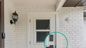 A white door with a window, a keypad lock, and a doorbell.