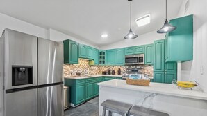 A modern kitchen with teal cabinets, stainless steel appliances, a marble island, and a coffee machine.