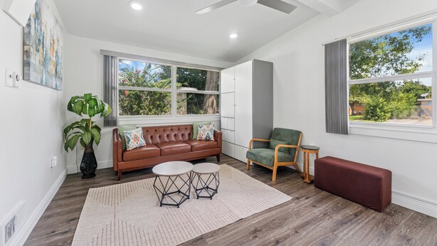 A modern living room with a brown leather sofa, a green armchair, a small round table, and a large window with a view of greenery.