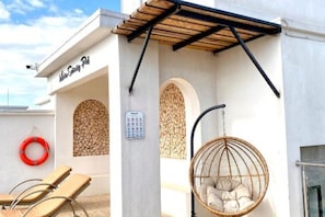 A building with a sign reading "Mare Galleria PIA," a wooden pergola, a hanging wicker chair, and a lifebuoy.