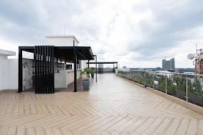 A rooftop terrace with a wooden floor, a black metal fence, and a white building in the background.
