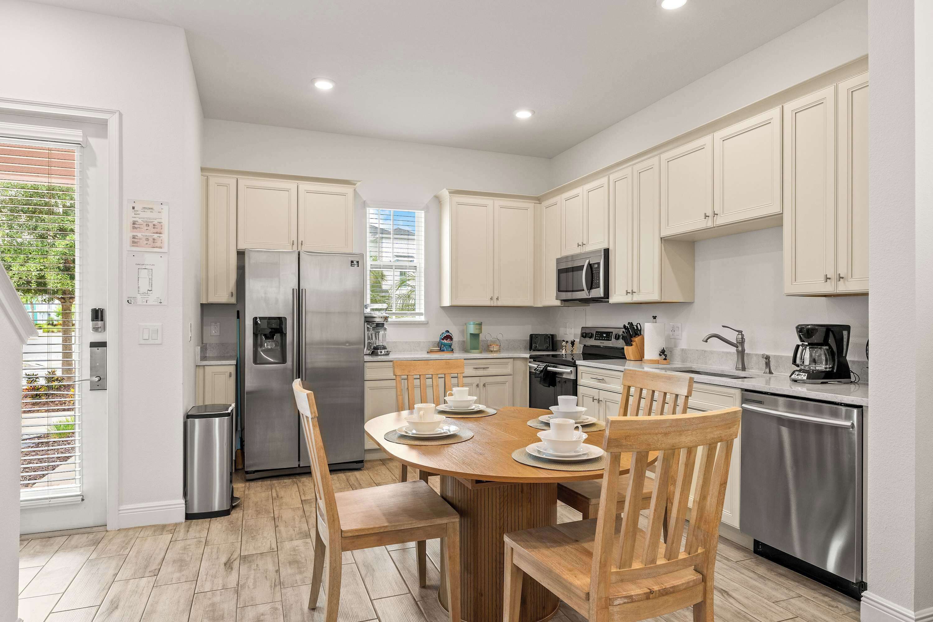 A modern kitchen with white cabinets, stainless steel appliances, and a dining area with wooden chairs and a table set for four.
