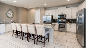A modern kitchen with a central island, stainless steel appliances, and a clock on the wall.