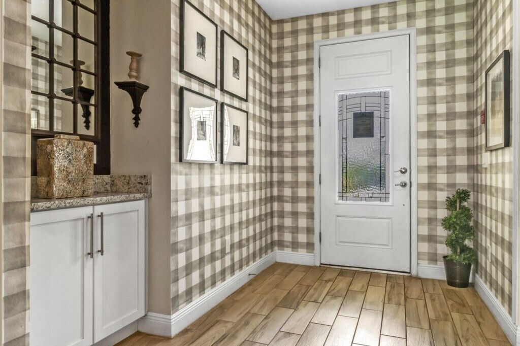 Un couloir avec un papier peint à carreaux, une porte blanche avec une fenêtre et une plante en pot.