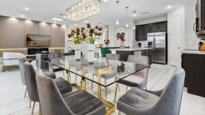 A modern kitchen with stainless steel appliances, a glass dining table, and contemporary chairs.