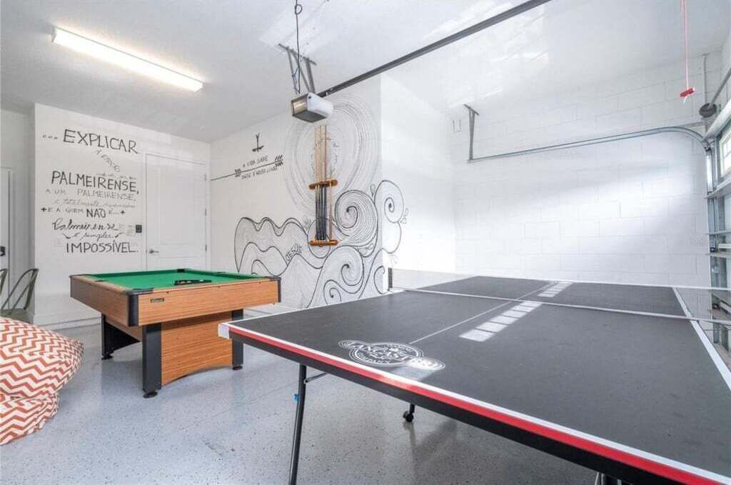 A billiards room with a pool table and a snooker table, white walls with decorative text, and a ceiling with exposed beams and lighting fixtures.