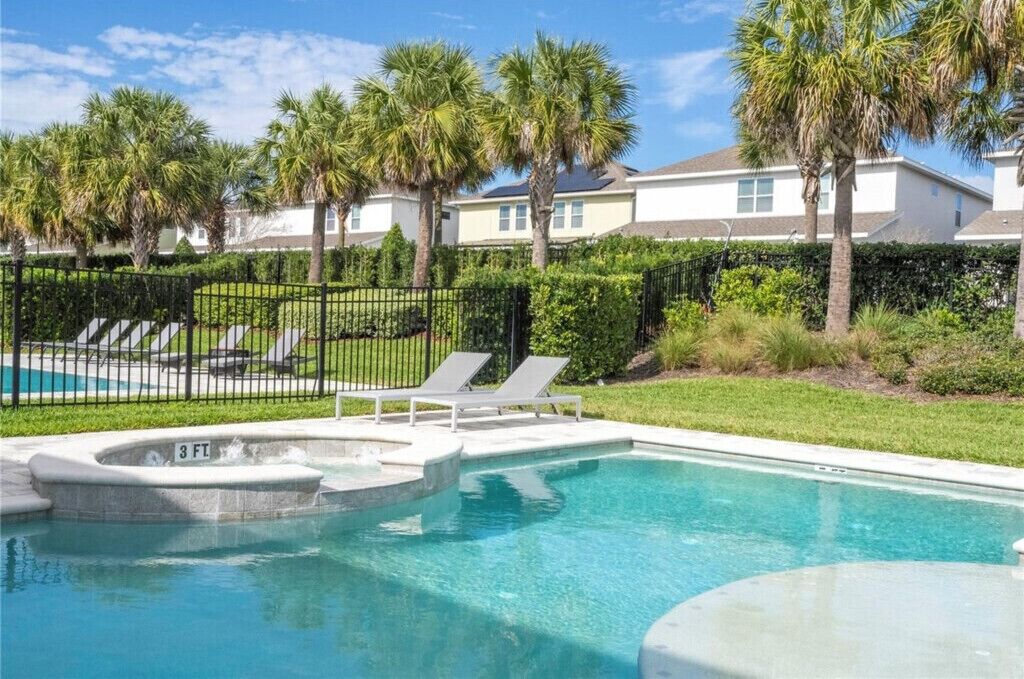 A swimming pool with lounge chairs, palm trees, and a fenced area.