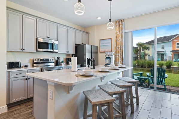 A modern kitchen with a large island, stainless steel appliances, and a view of a residential area.