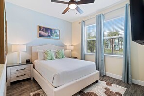 A bedroom with a bed, nightstands, a ceiling fan, a window with curtains, and a painting on the wall.