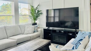 A modern living room with a large flat-screen TV, a beige sofa, a coffee table, and a potted plant. - “AH!” It's time to relax at the beach! (Avon)